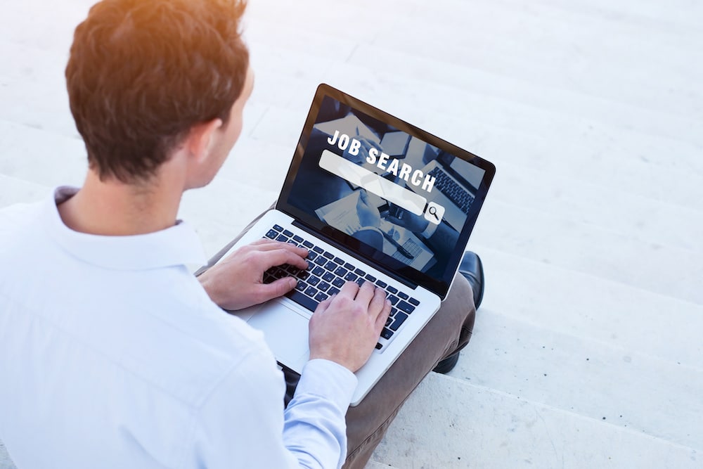 A young man on his laptop and working on searching for a new job by allegiance staffing.