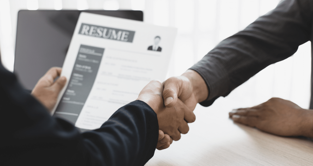 Job applicant shaking hands with a prospective employer reviewing his resume