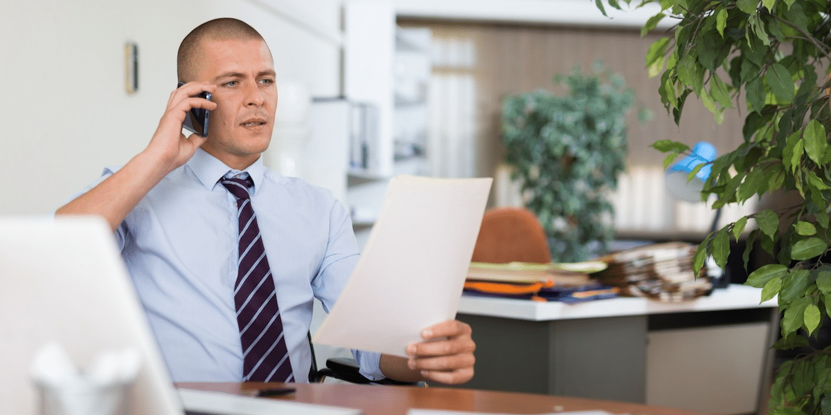 Office worker sitting at his desk on the phone while holding a piece of paper